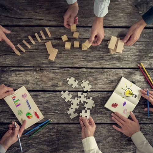 47522195 - businesspeople organizing business strategy while holding puzzle pieces, writing down ideas on paper and rearranging wooden blocks. concept of brainstorming, management, innovation or creativity.